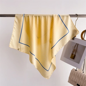Detail view of the lightweight yellow silk-like scarf with white polka dots and blue border