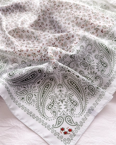 Detail of paisley print silk scarf showing white fabric with green patterns and soft sheen