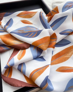 Detail view of smooth silk scarf with orange and blue leaf patterns on white background