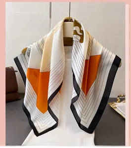 Detail of silk-feel scarf featuring geometric orange, beige, and black block patterns