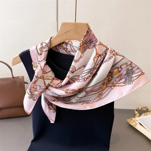 Pink silk-like scarf with gold chain and buckle patterns draped on a wooden hanger