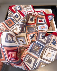 Detailed view of geometric herringbone silk scarf with red border in luxury packaging