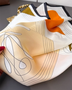 Close-up of abstract orange and beige silk scarf showing satin texture and fine stitching