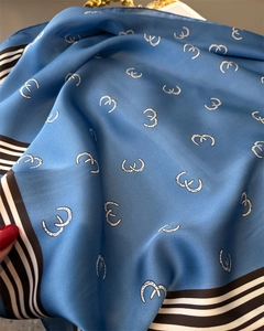 Detailed view of blue silk scarf featuring white horseshoe prints and striped edges