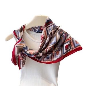 Elegant geometric print scarf with red borders draped over a white vest for styling