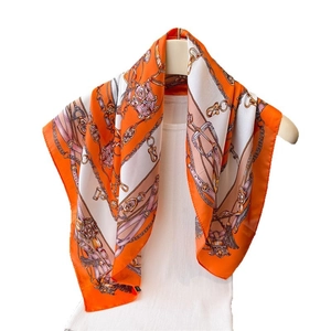 Orange silk square scarf featuring chain buckle print draped on a white vest