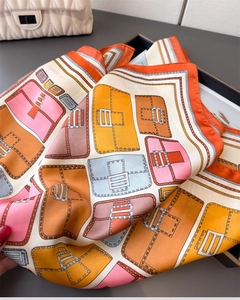 Detailed view of colorful luxury handbag print on a glossy silk scarf with orange hem