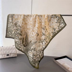 Detailed close-up of olive green silk scarf with floral and bird print patterns