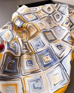 Close-up of silk-like scarf featuring blue geometric prints and a yellow border detail