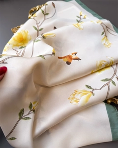 Detailed texture of silk scarf featuring floral bird prints and dark green rolled edges