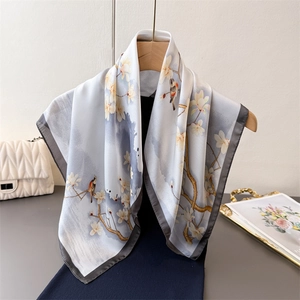 Satin silk scarf with magnolia and bird print draped over a black knit sweater
