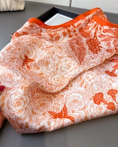 Detail of silk-like square scarf featuring orange floral patterns and bird motifs
