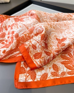 Macro detail of orange and white floral silk scarf showing premium satin texture and hem