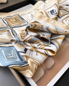 Detailed view of silky satin scarf featuring blue and gold geometric print on a tray