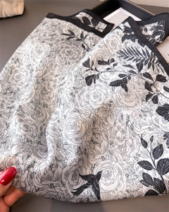 Detail of soft silk-like square scarf featuring black floral and bird prints on white base