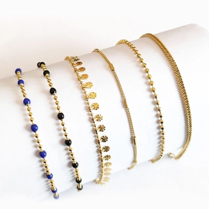 Set of six varied 18K gold-plated stainless steel bracelets on white cylindrical displays