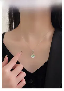 Détail d'un pendentif goutte évidé avec motif floral vert porté sur une chaîne argent