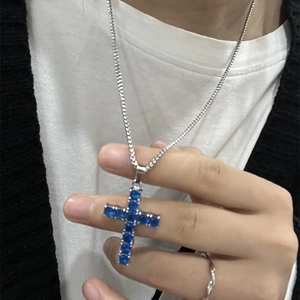 Detail of silver cross necklace featuring deep blue square zircons on model neck