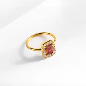 Détail d'une bague dorée avec zircon rouge rectangulaire et entourage de cristaux fins