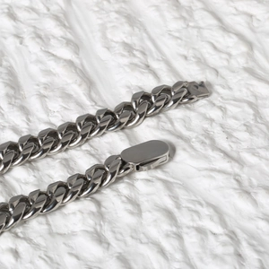 Close-up of polished stainless steel Cuban link chain on a textured stone background