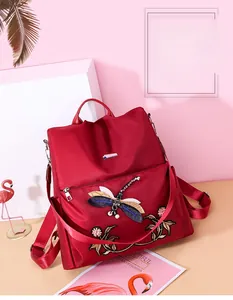 Detail of red waterproof nylon backpack featuring dragonfly embroidery and pearl accents