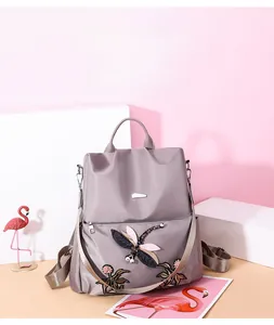 Detail of grey oxford backpack featuring floral dragonfly embroidery and metal zippers