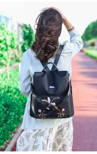 Outdoor shot of a black nylon backpack featuring colorful dragonfly and floral embroidery