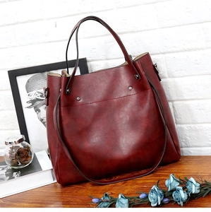 Detalle de bolso tote vintage en ecopiel burdeos con remaches sobre mesa de madera rústica