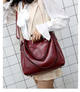 Detalle de bolso tote de cuero granate con asas dobles y correa de hombro ajustable