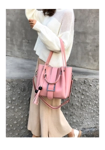 Rosafarbene Eimertasche mit Quastenanhänger, getragen mit einem weißen Strickpullover