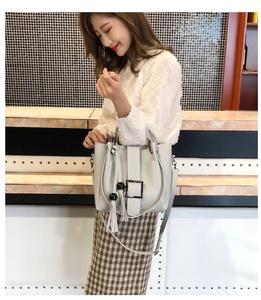 Graue Eimertasche mit Metallschnalle und Quastenanhänger an einem Modell