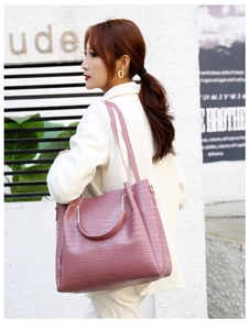 Detailed side view of an embossed crocodile texture handbag with gold metal handles