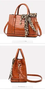 Detail of yellow-brown crocodile embossed handbag with leopard scarf and gold hardware