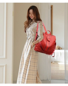 Red embossed woven leather backpack with adjustable straps worn by a model in a dress