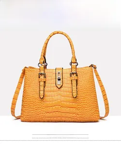 Détail de face d'un sac à main jaune à motif crocodile avec fermoir en métal et anses