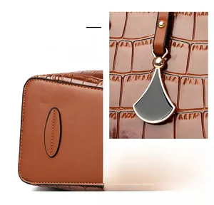 Detail of brown crocodile embossed leather handbag with fan-shaped pendant and base studs