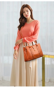 Detailed view of orange crocodile pattern handbag with gold hardware on fashion model