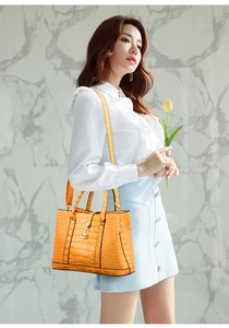 Detail of bright orange crocodile pattern handbag with gold metal lock and shoulder strap