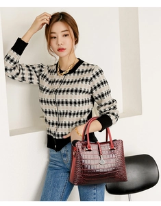 Detail of burgundy crocodile-embossed handbag with silver drop pendant held by model
