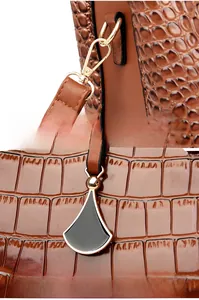 Detail of brown crocodile pattern handbag showing gold hardware hook and enamel pendant