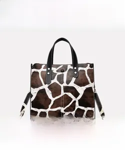 Detailed view of the giraffe print tote bag with black leather handles and silver rivets