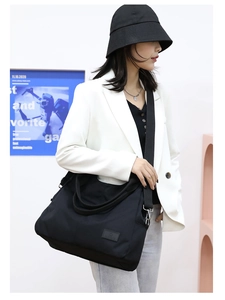 Black nylon tote bag featuring a leather brand patch and adjustable shoulder strap