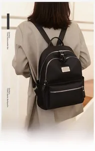 Detailed back view of a black oxford fabric backpack with silver zippers on a model
