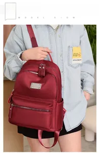 Detail view of the deep red waterproof nylon backpack worn by a model in casual style