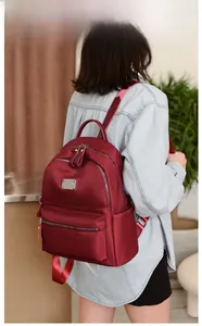 Detailed back view of a burgundy waterproof nylon backpack worn by a model in a cozy room