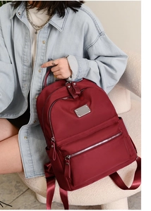 Detail view of burgundy nylon backpack with silver zippers and wide woven straps