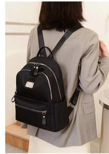 Rear view of a casual black Oxford fabric backpack with silver zippers on a female model