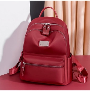 Detail of burgundy oxford fabric backpack with silver zippers and metal plaque accents