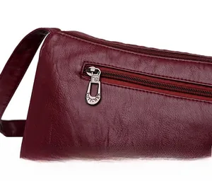 Dettaglio della cerniera in metallo dorato e della pelle martellata della borsa bordeaux