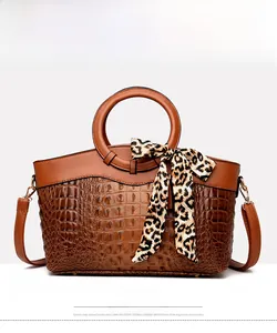Detailed front view of tan crocodile pattern handbag with silk scarf and round handle